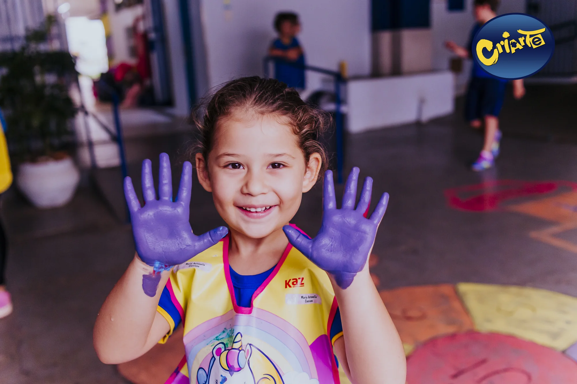 Criança da Educação Infantil mostrando as mãos coloridas durante atividade artística